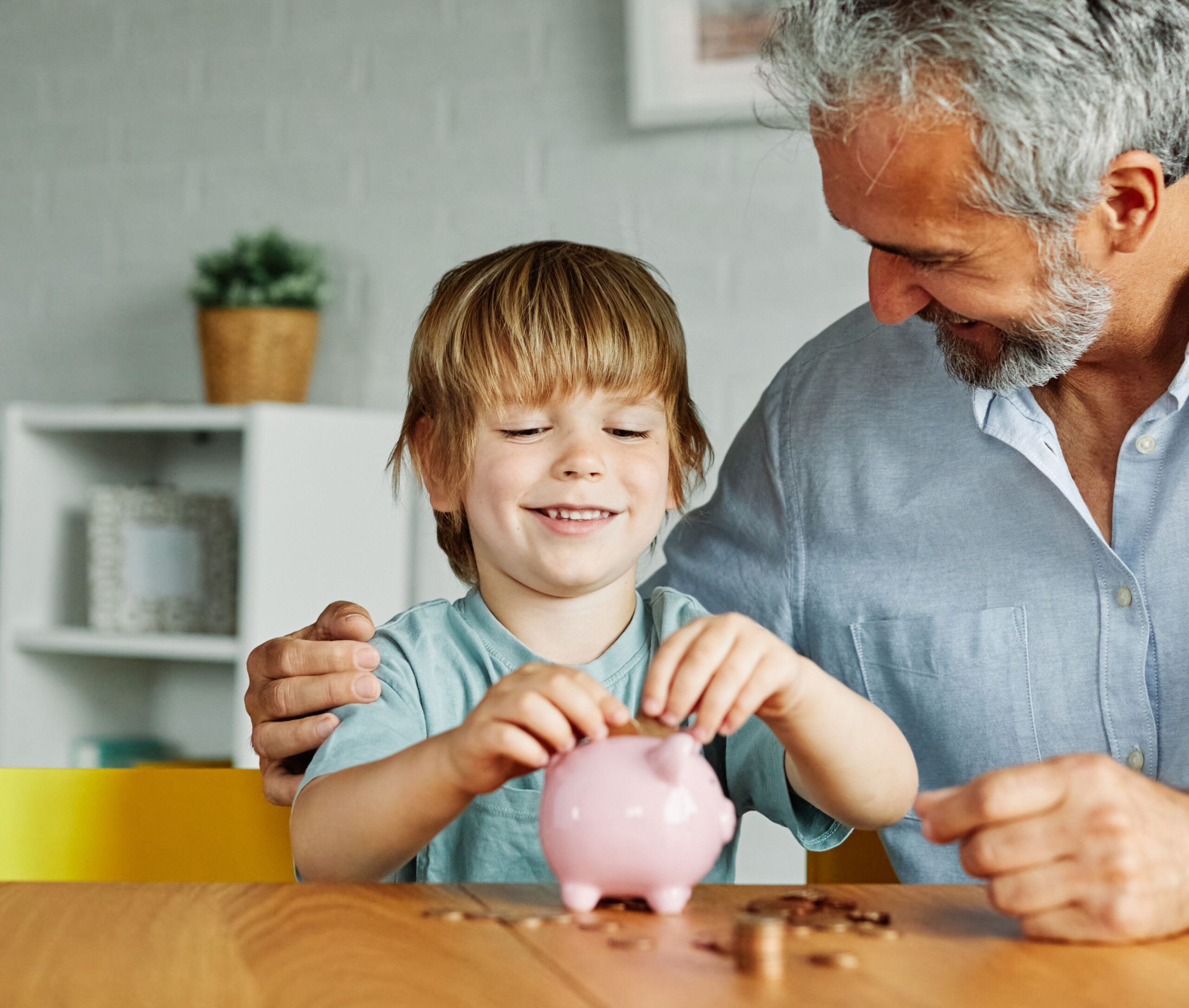 Grandfather and grandson put money in piggy bank.